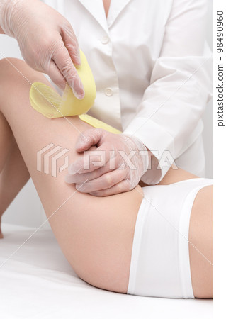 Master hands in gloves removing hair on women leg. Depilation procedure with green hot wax in professional beauty salon. Part of photo series. 98490960