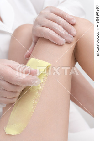 Closeup view of cosmetologist removing hair on female leg using hot wax in professional beauty salon. Depilation with hot wax in beauty salon. Part of photo series. Closeup view of cosmetologist removing hair on female leg using hot wax in professional beauty salon. Depilation with hot wax in beauty salon. Part of photo series. 98490997