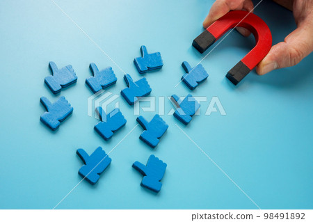 A hand with a magnet attracts social media like symbols. 98491892