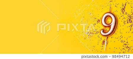 Gold candle in the form of number nine on yellow background with confetti. 98494712