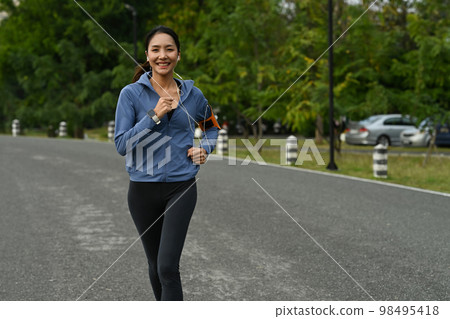 Shot of asian woman in sportswear and earphones jogging in public park. Fitness, sport and healthy lifestyle concept Shot of asian woman in sportswear and earphones jogging in public park. Fitness, sport and healthy lifestyle concept 98495418