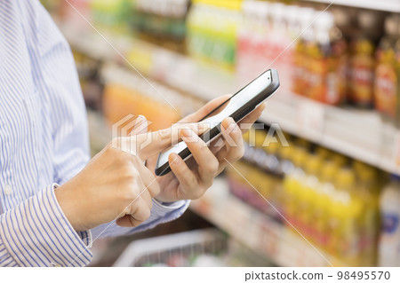 Middle female hand operating a smartphone while shopping at a supermarket Middle female hand operating a smartphone while shopping at a supermarket 98495570