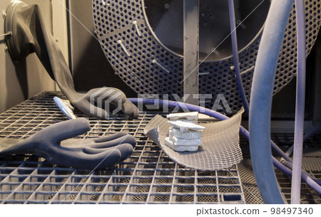 Models printed on a 3D printer from white polyamide powder inside a shot blasting machine for cleaning. Inside Shot blasting machine. Open machine for shot blasting of objects. Industrial machine Models printed on a 3D printer from white polyamide powder inside a shot blasting machine for cleaning. Inside Shot blasting machine. Open machine for shot blasting of objects. Industrial machine 98497340