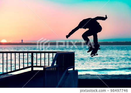 Unrecognizable teenage boy silhouette showing high jump tricks on scooter against 98497746