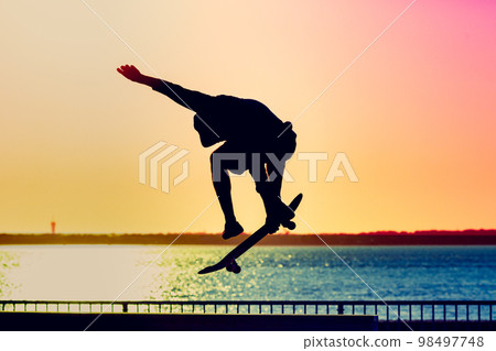 Unrecognizable teenage boy silhouette showing high jump tricks on scooter against Unrecognizable teenage boy silhouette showing high jump tricks on scooter against 98497748