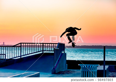 Unrecognizable teenage boy silhouette showing high jump tricks on scooter against Unrecognizable teenage boy silhouette showing high jump tricks on scooter against 98497803