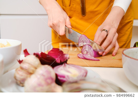Closeup view of female hands slicing onion Closeup view of female hands slicing onion 98499662