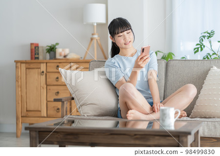 一個坐在客廳沙發上看著她的智能手機的女高中生 一個坐在客廳沙發上看著她的智能手機的女高中生 98499830