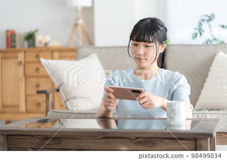 一個高中女生在客廳裡用智能手機看視頻 一個高中女生在客廳裡用智能手機看視頻 98499834