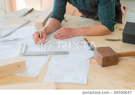 A portrait of a carpenter in goggles and work overalls draws a blueprint for a workshop. A portrait of a carpenter in goggles and work overalls draws a blueprint for a workshop. 98500647