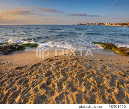 black sea shore at sunrise. vacation and leisure background. landscape with rock on the sand and town in the distance on the horizon line on a sunny morning black sea shore at sunrise. vacation and leisure background. landscape with rock on the sand and town in the distance on the horizon line on a sunny morning 98501010