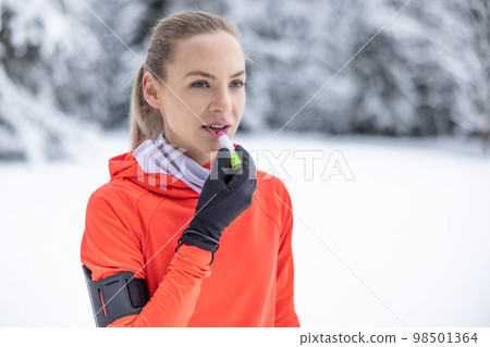 A young female runner applies protective balm to her lips due to the frosty weather, prevention of chapped and dry lips 98501364
