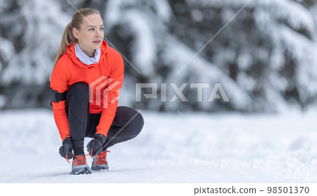An attractive female runner is tying her shoelaces before training on the snow in the winter season. An attractive female runner is tying her shoelaces before training on the snow in the winter season. 98501370