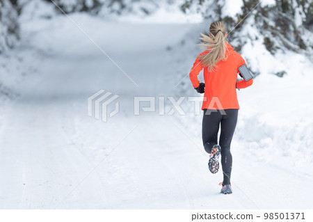 Running in winter, rear view of a female runner on a snowy path in a park or forest Running in winter, rear view of a female runner on a snowy path in a park or forest 98501371