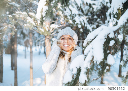 Happy blonde woman in winter clothes hands near face in snowy winter forest Happy blonde woman in winter clothes hands near face in snowy winter forest 98501632