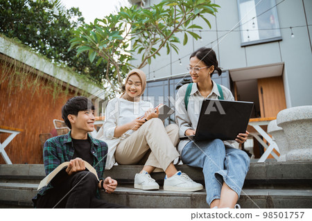 Three young asian college students using laptops sitting on stairs Three young asian college students using laptops sitting on stairs 98501757