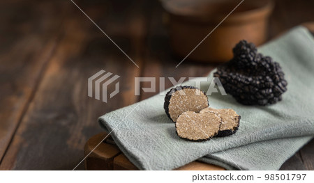 Whole and sliced black truffles mushroom on wooden board on green napkin, close up 98501797