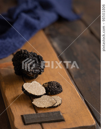 Whole and sliced black truffles mushroom on wooden board on dark brown table, close up 98501806