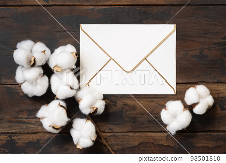 Blank envelope with cotton flowers top view on dark brown wood, wedding mockup 98501810