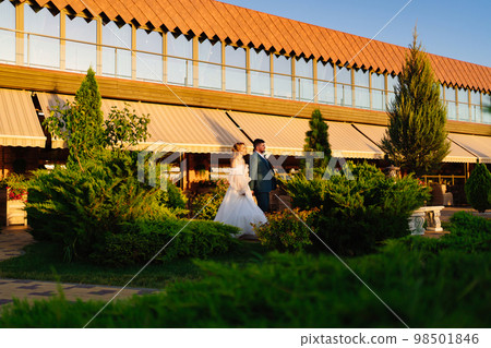 the bride and groom walk holding hands along the path the bride and groom walk holding hands along the path 98501846