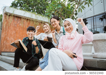 Smiling young people with fists raised while sitting on steps Smiling young people with fists raised while sitting on steps 98501940