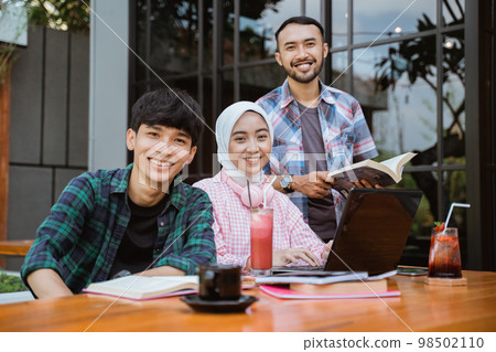 three smiling Asian students looking at camera while studying together 98502110