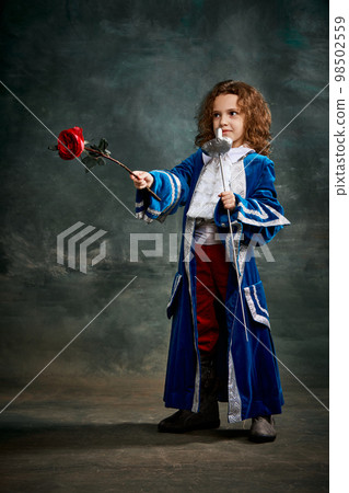 Emotional kid, little girl wearing costume of prince, musketeer and royal person posing over dark vintage style background. Fashion, theater, beauty, emotions concept Emotional kid, little girl wearing costume of prince, musketeer and royal person posing over dark vintage style background. Fashion, theater, beauty, emotions concept 98502559