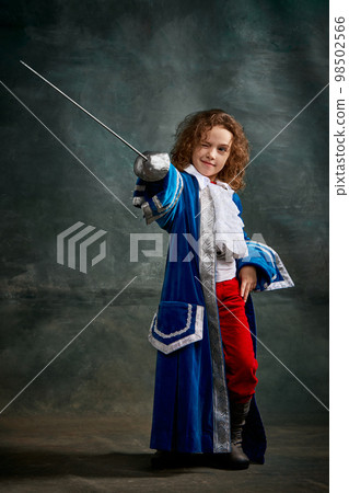 Emotional kid, little girl wearing costume of prince, musketeer and royal person posing over dark vintage style background. Fashion, theater, beauty, emotions concept Emotional kid, little girl wearing costume of prince, musketeer and royal person posing over dark vintage style background. Fashion, theater, beauty, emotions concept 98502566