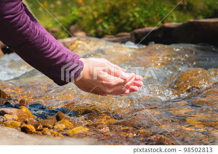 man takes clean water from a stream in the forest. Hand close up. Sunny summer day in the forest. Beautiful spring water flows in the rocks man takes clean water from a stream in the forest. Hand close up. Sunny summer day in the forest. Beautiful spring water flows in the rocks 98502813