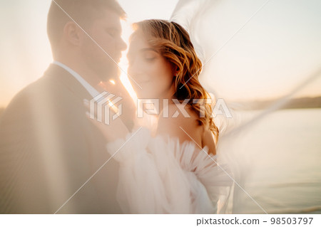 the bride and groom under the veil on the sunset by the river 98503797