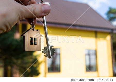 A hand with the keys to a new house on the background of an unfinished cottage. Building, project, moving to a new home, mortgage, rent and purchase real estate. To open the door. Copy space A hand with the keys to a new house on the background of an unfinished cottage. Building, project, moving to a new home, mortgage, rent and purchase real estate. To open the door. Copy space 98504044