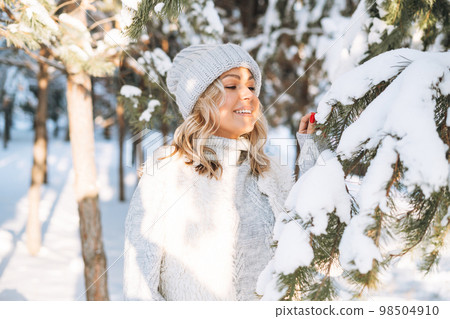 Happy blonde woman in winter clothes hands near face in snowy winter forest Happy blonde woman in winter clothes hands near face in snowy winter forest 98504910