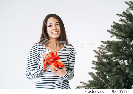 Young smiling asian woman with gift box in hands with Christmas tree on white background isolated Young smiling asian woman with gift box in hands with Christmas tree on white background isolated 98505154