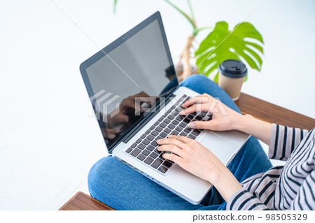 Hands of a woman working on a computer in a bright white living room Hands of a woman working on a computer in a bright white living room 98505329