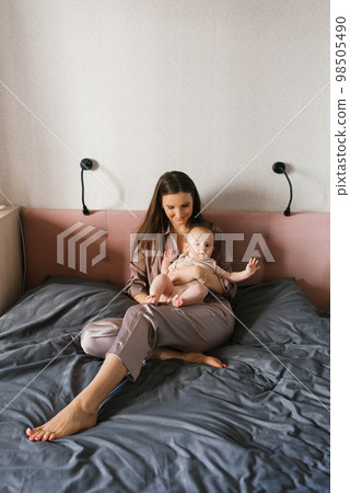 Happy mother holds a baby baby in her arms, smiling, sitting on the bed Happy mother holds a baby baby in her arms, smiling, sitting on the bed 98505490