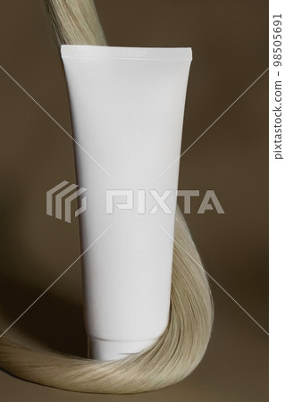 A strand of natural dark hair for extensions with a bottle of care product. A strand of natural dark hair for extensions with a bottle of care product. 98505691