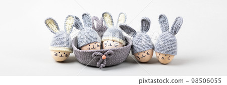 Five Easter eggs with funny faces and gray crocheted hats with bunny ears in a decorative basket on a gray background. Happy Easter concept. Banner Five Easter eggs with funny faces and gray crocheted hats with bunny ears in a decorative basket on a gray background. Happy Easter concept. Banner 98506055