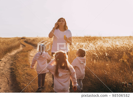 Mother and daughters triplets family time, blowing bubbles at sunset outdoors Mother and daughters triplets family time, blowing bubbles at sunset outdoors 98506582