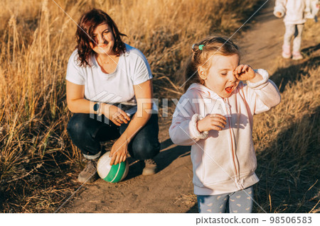 Mom with ball on walk with twins. girl is crying. Kids tantrums at street. Upset baby boy at park. Childhood. 98506583