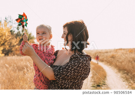 Mom shows little daughter how to use a windmill on outdoor. ESG and Clean Energy Concept. 98506584