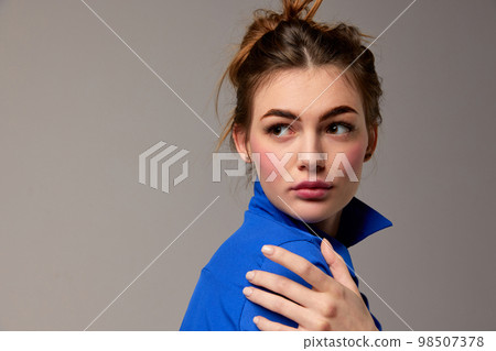 Fashionable stylish emotional woman wearing blue shirt posing over gray background. Model with vivid facial expression. Concept of fashion, style, youth, beauty Fashionable stylish emotional woman wearing blue shirt posing over gray background. Model with vivid facial expression. Concept of fashion, style, youth, beauty 98507378