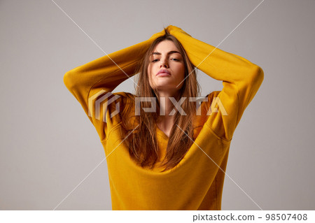 Half-length portrait of fashionable sensual emotional woman wearing trendy yellow sweater posing over gray background. Concept of fashion, style, youth, beauty Half-length portrait of fashionable sensual emotional woman wearing trendy yellow sweater posing over gray background. Concept of fashion, style, youth, beauty 98507408