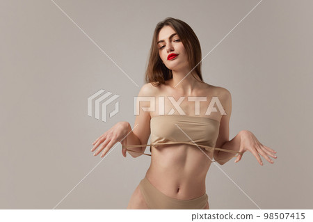 Portrait of tender sensual young woman wearing nude color underwear isolated over grey background. Girl with red lipstick. Accent makeup Portrait of tender sensual young woman wearing nude color underwear isolated over grey background. Girl with red lipstick. Accent makeup 98507415