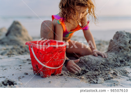 Little girl playing on the beach, building sand castle. 98507610