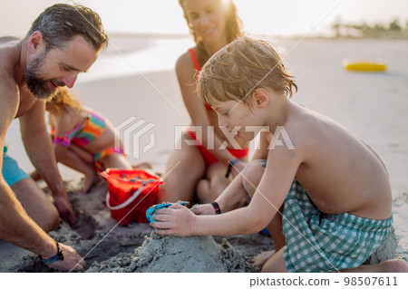 Happy family with little kids enjoying time at sea in exotic country, building sand castle. 98507611