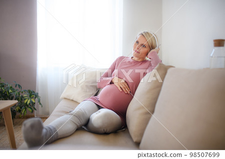 Pregnant woman sitting in her bed, listening music and enjoying time for herself. 98507699