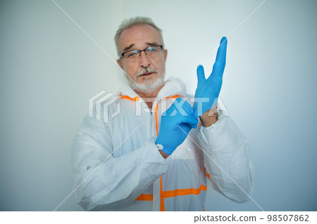 Portrait of doctor in protective coveral putting on surgical gloves. 98507862