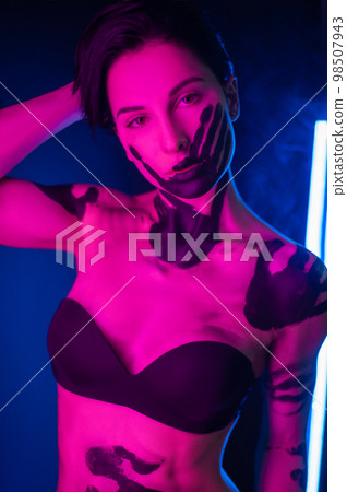 sexy girl in underwear smeared with black paint in bright neon light on a dark background 98507943