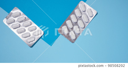 Oval white pills in a gray blister pack on a blue background, top view. 98508202
