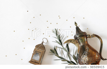 Ramadan Kareem setting. Arabic dallah coffee pot, golden ornamental Moroccan lantern. Green oluve tree branches, star confetti isolated on white table background. Iftar party celebration, Eid ul Fitr Ramadan Kareem setting. Arabic dallah coffee pot, golden ornamental Moroccan lantern. Green oluve tree branches, star confetti isolated on white table background. Iftar party celebration, Eid ul Fitr 98509415